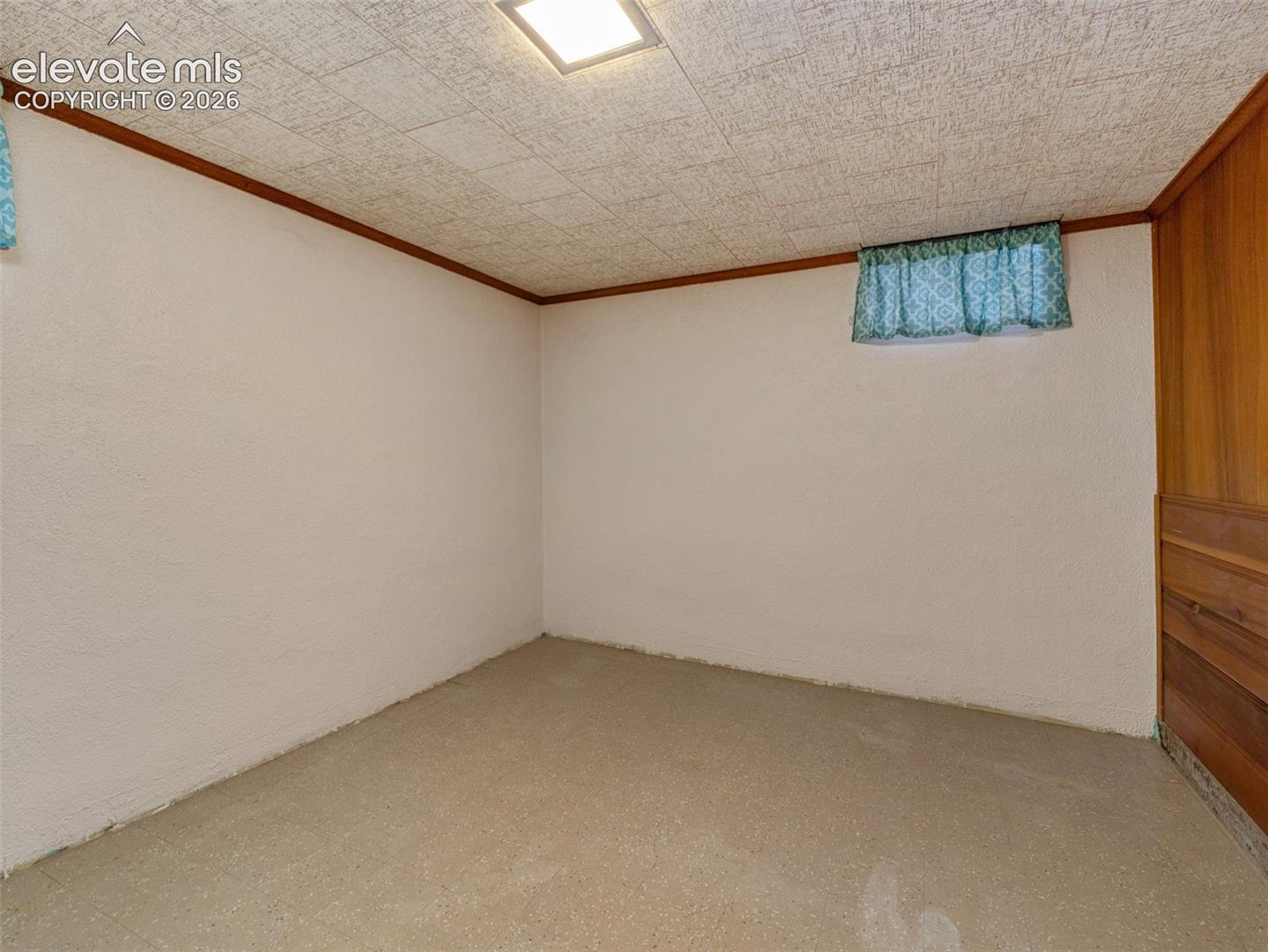 Textured ceiling featuring a flush-mount light fixture, high-set window, and wood-paneled wall accent