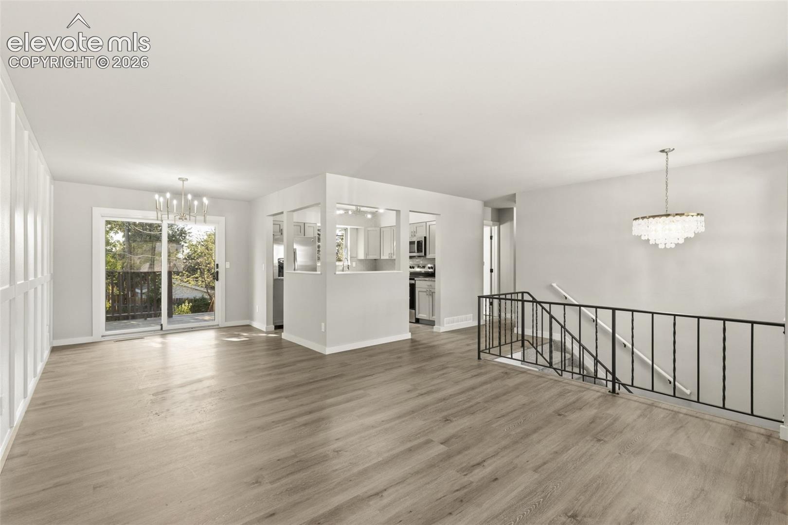 Open living space featuring luxury vinyl plank flooring, a contemporary tiered chandelier, and a sliding glass door leading to an exterior deck