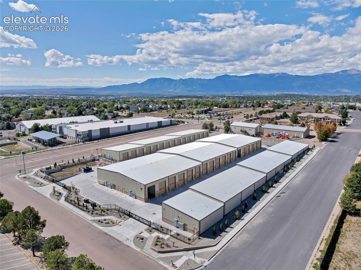 Multiple industrial buildings with metal siding and roofs, surrounded by paved roadways and landscaping