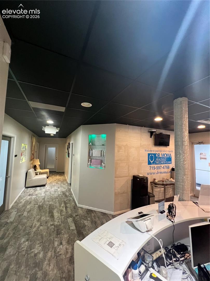 Reception area featuring wood-finish flooring, a dark-toned drop ceiling with recessed lighting, a built-in illuminated wall niche, and a decorative textured column