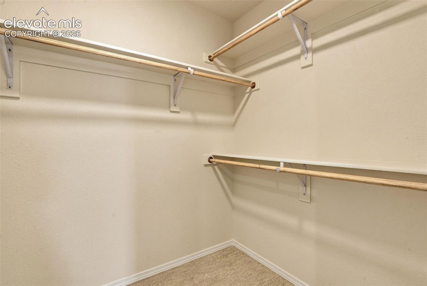 Walk-in closet featuring multi-level wood-finish shelving and integrated hanging rods with white support brackets