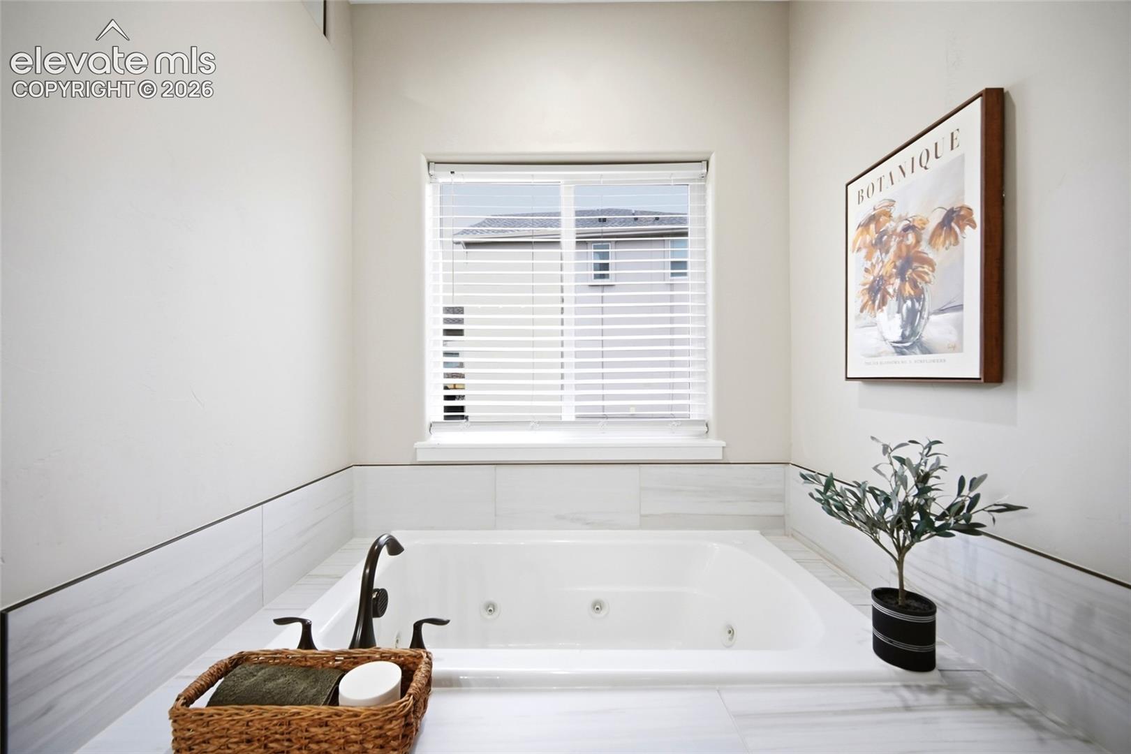 Built-in jetted soaking tub surrounded by large-format tile wainscoting and a center-positioned window with horizontal blinds