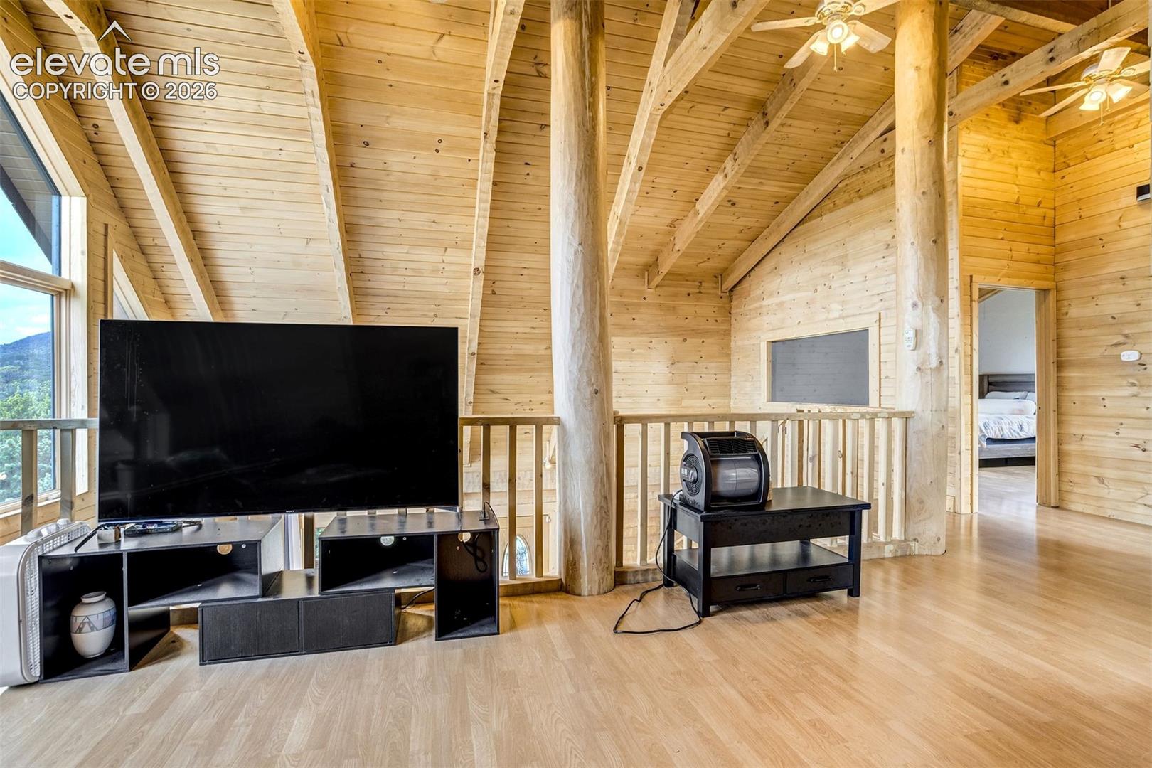 Vaulted ceiling with exposed wood beams, natural wood plank walls, light wood-finish flooring, and a railing overlooking a lower level