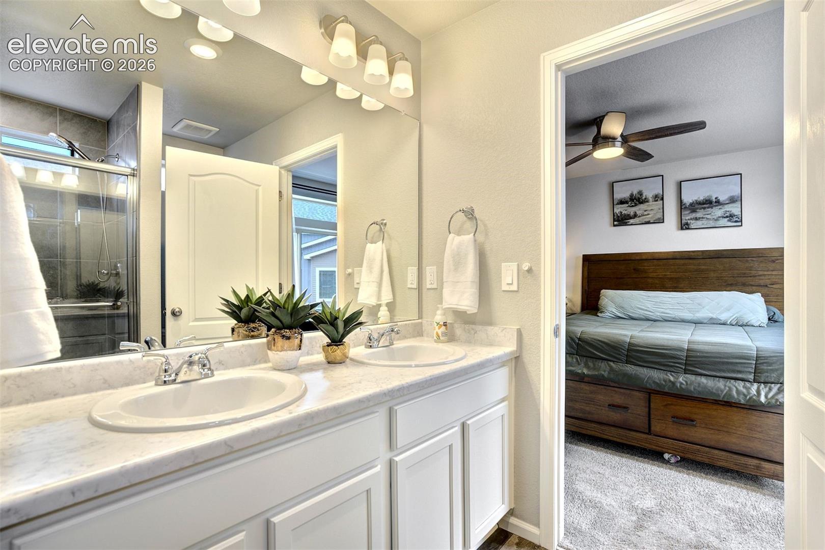 Bathroom vanity featuring double integrated oval sinks, white cabinetry, a stone-finish countertop, a full-width mirror, and multi-bulb vanity lighting