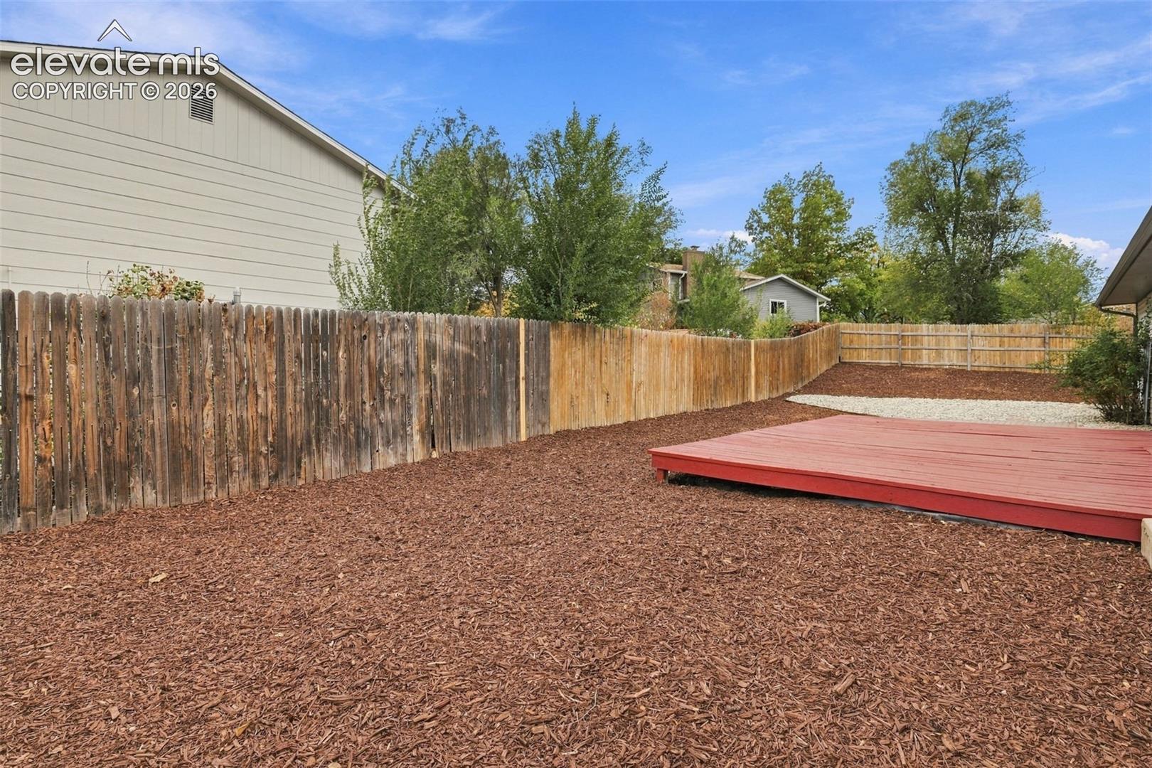 Backyard featuring a red-painted wood deck, mulch ground cover, and a wood privacy fence
