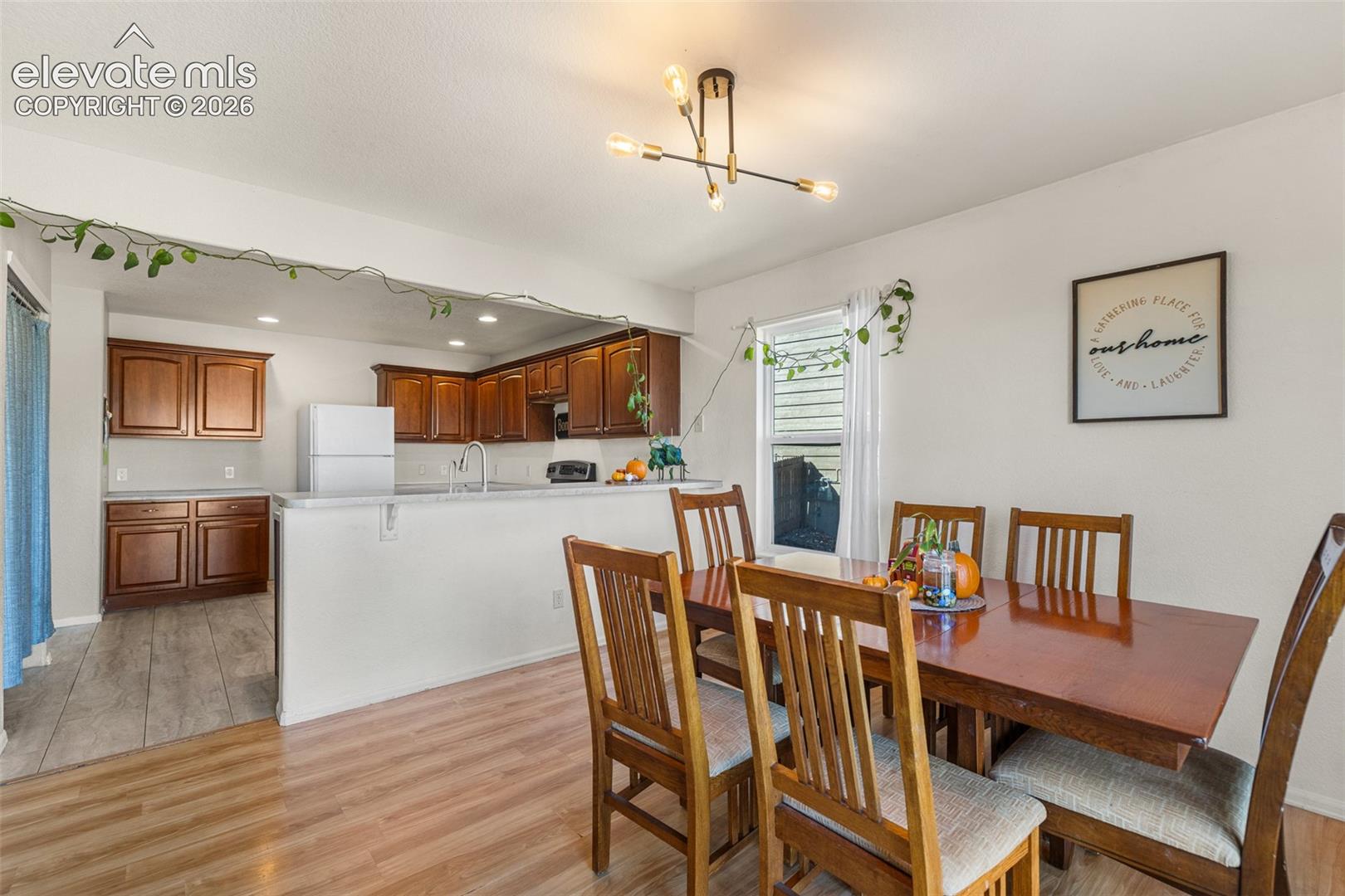 Kitchen featuring wood cabinetry, recessed lighting, and a breakfast bar counter, complemented by wood-finish flooring and a multi-arm modern light fixture