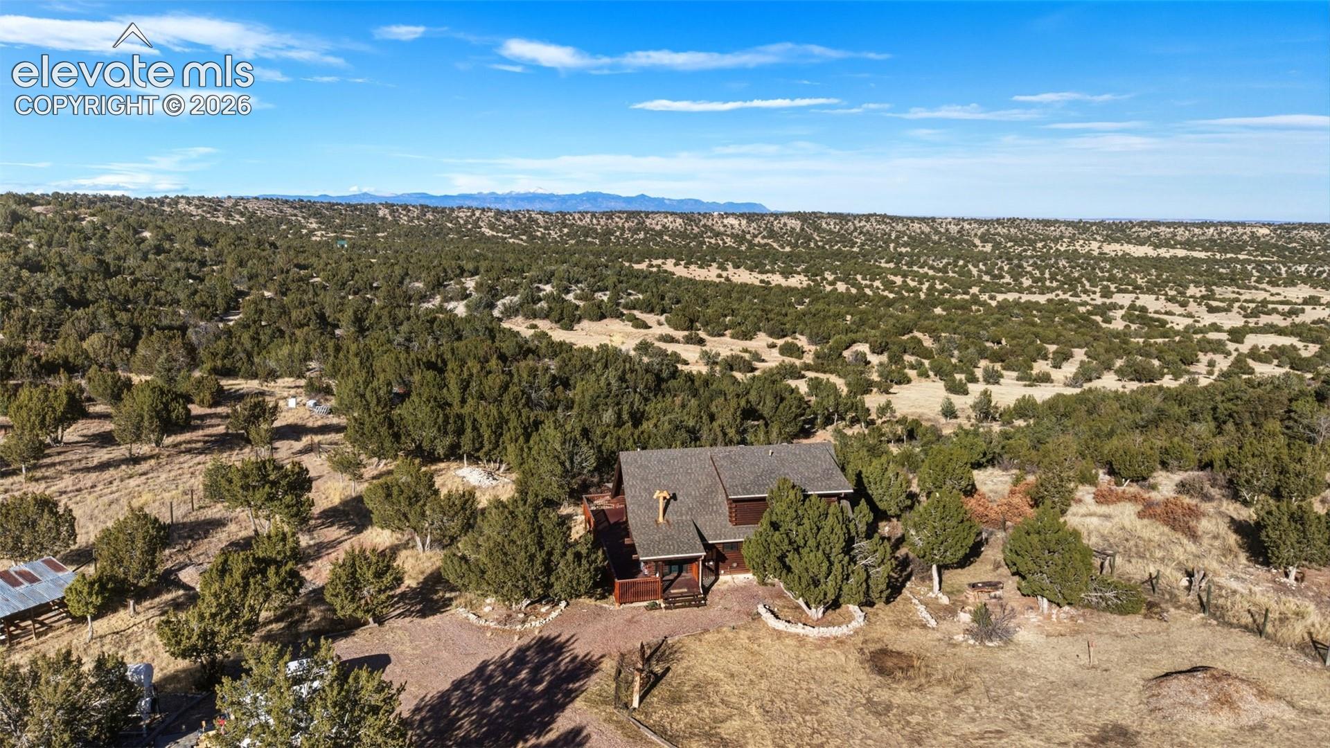 Expansive surrounding landscape with abundant foliage, a gravel driveway, and a multi-level structure with a dark roof