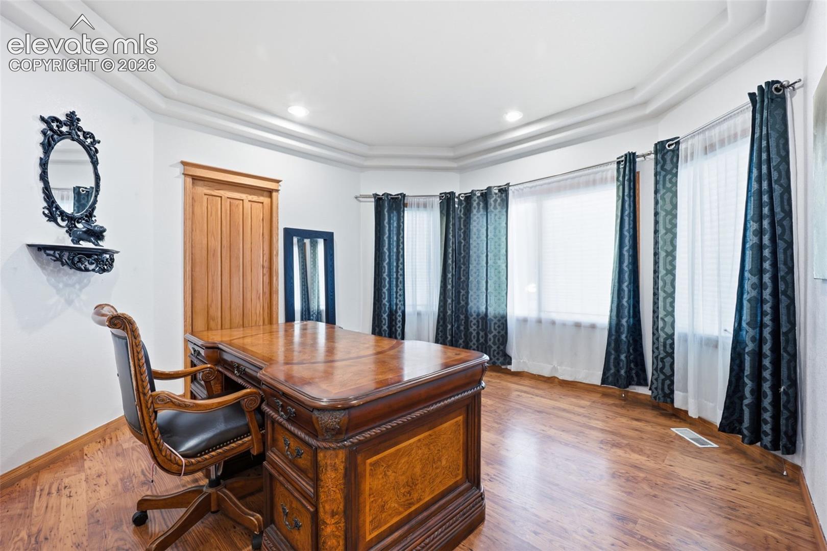 Curved bay windows, recessed ceiling lighting, wood-finish flooring, and a natural wood door
