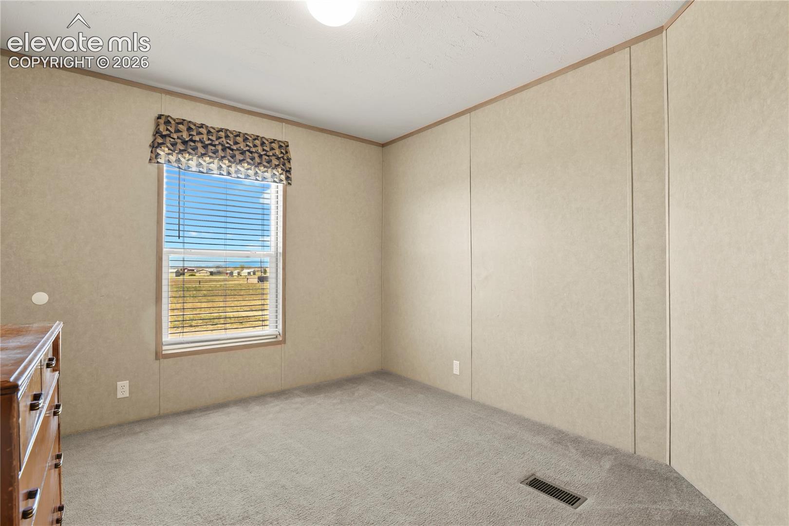 Neutral wall paneling, wall-to-wall carpeting, and a single-hung window with a textured fabric valance