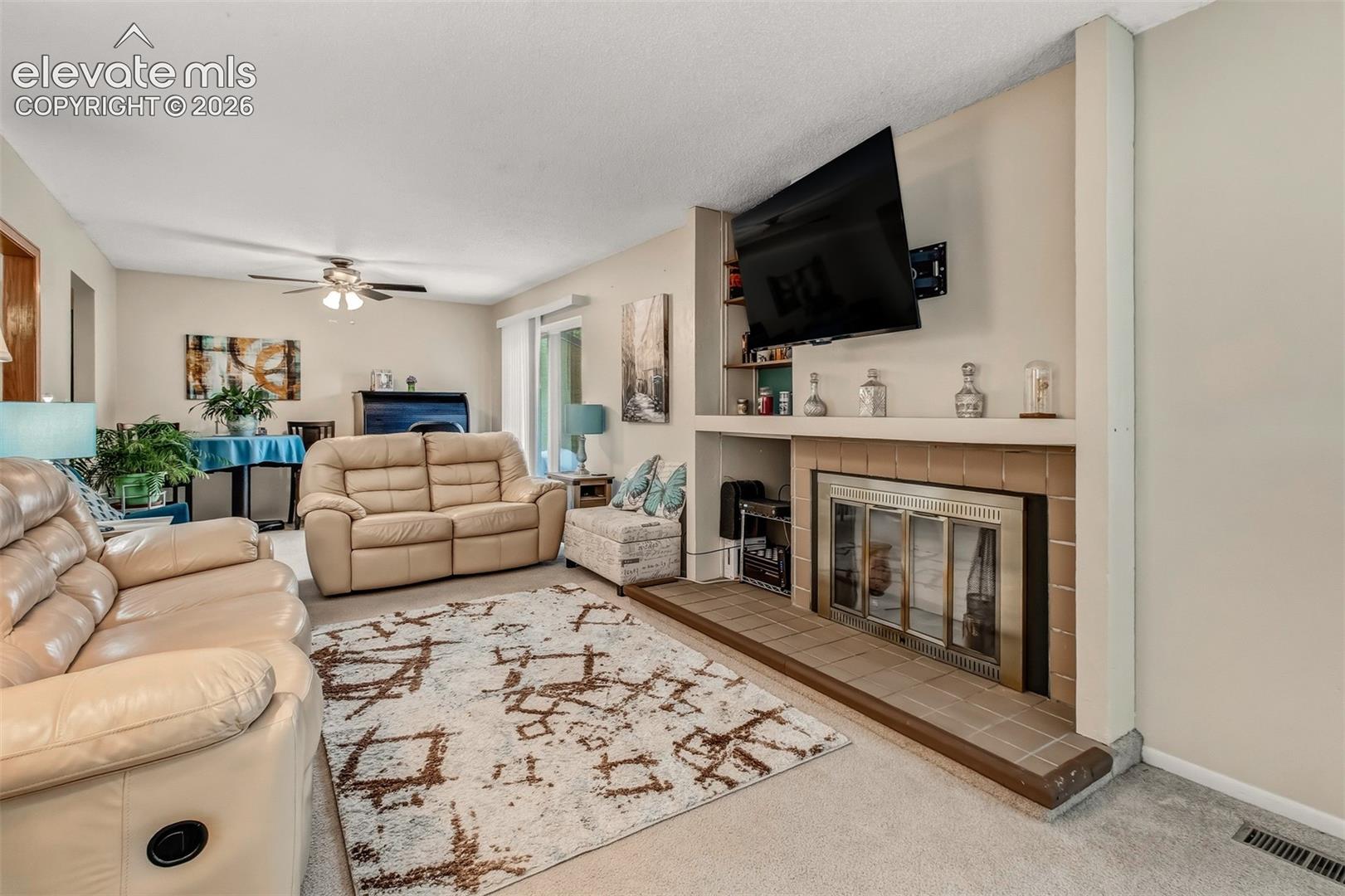 Fireplace with a metal screen surround, tile hearth, and built-in shelving, complemented by a ceiling fan