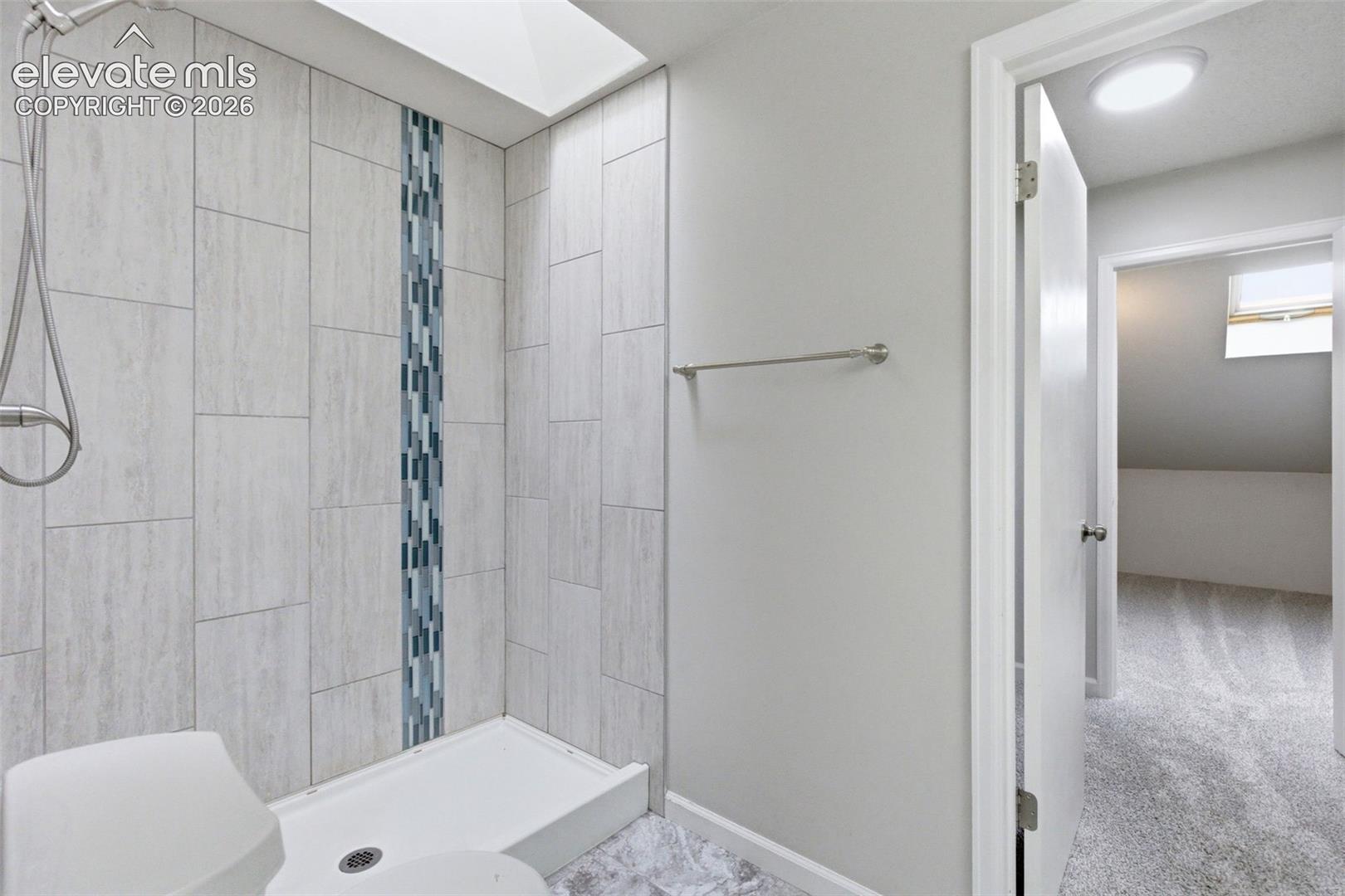 Shower with light-toned tiled walls, a decorative vertical accent stripe, and a white shower pan