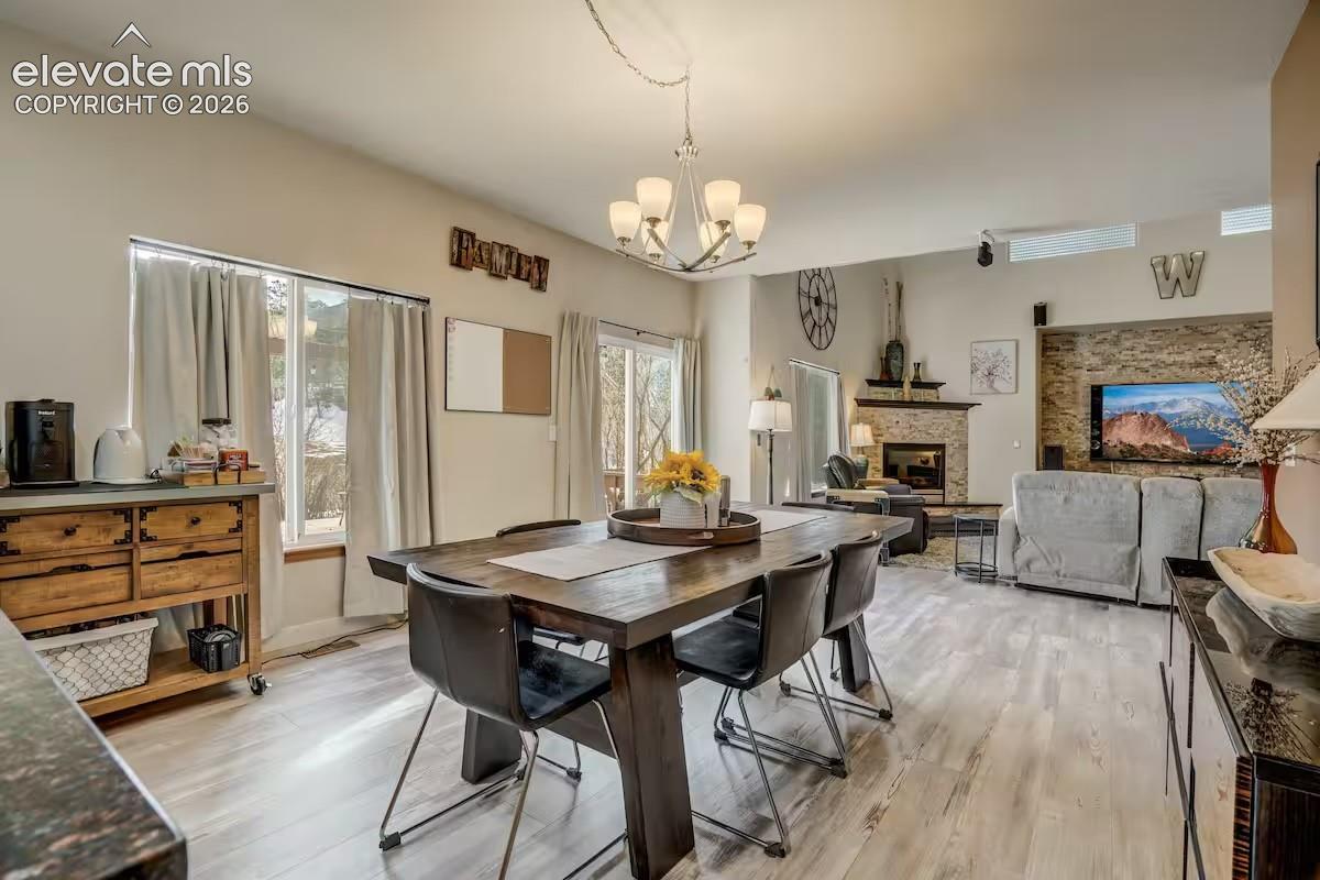 Open-concept living space featuring wood-finish flooring, a contemporary chandelier, a stone fireplace, and a sliding glass door