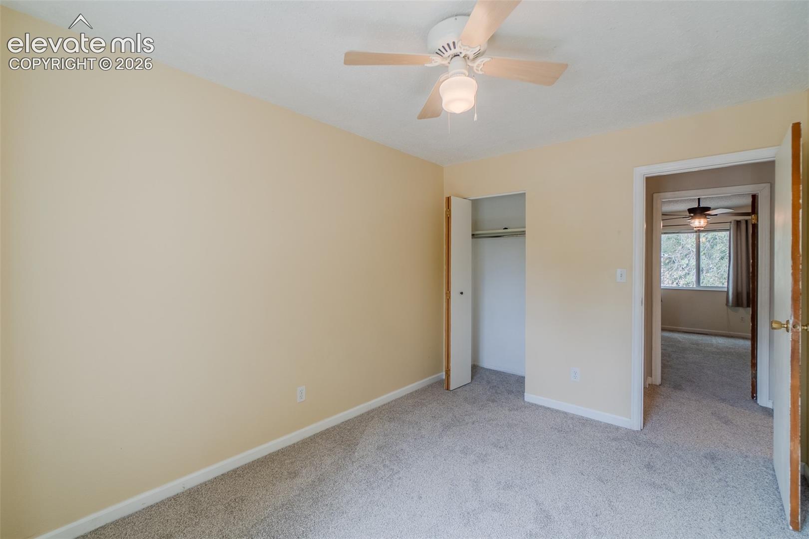 Neutral tone wall paint, light gray carpet flooring, ceiling fan with light fixture, bifold closet doors, and wood-finish interior door
