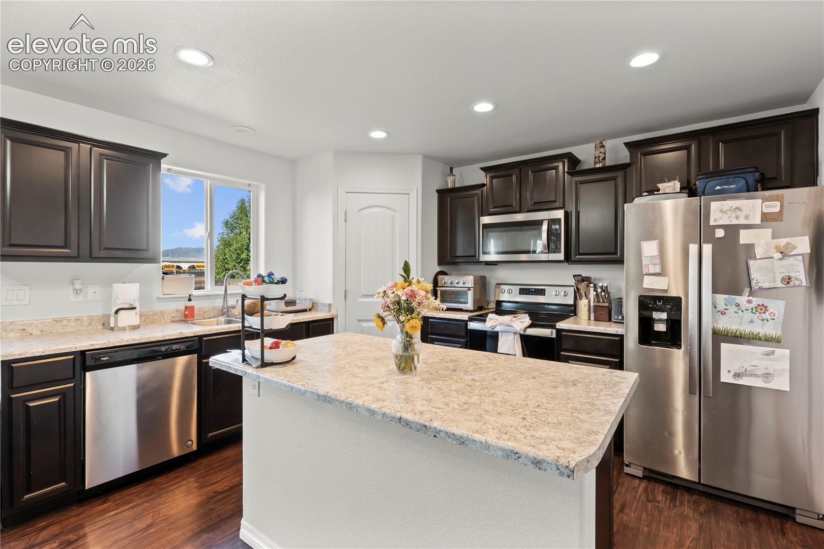 Kitchen featuring dark-finish cabinetry, stone-style countertops, a central island, stainless steel appliances, and wood-finish flooring