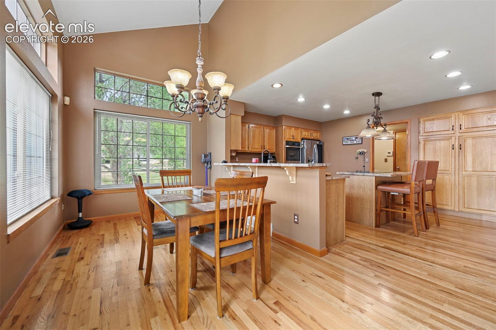 Vaulted ceiling with a decorative chandelier, expansive windows, wood-finish flooring, built-in cabinetry, and recessed lighting