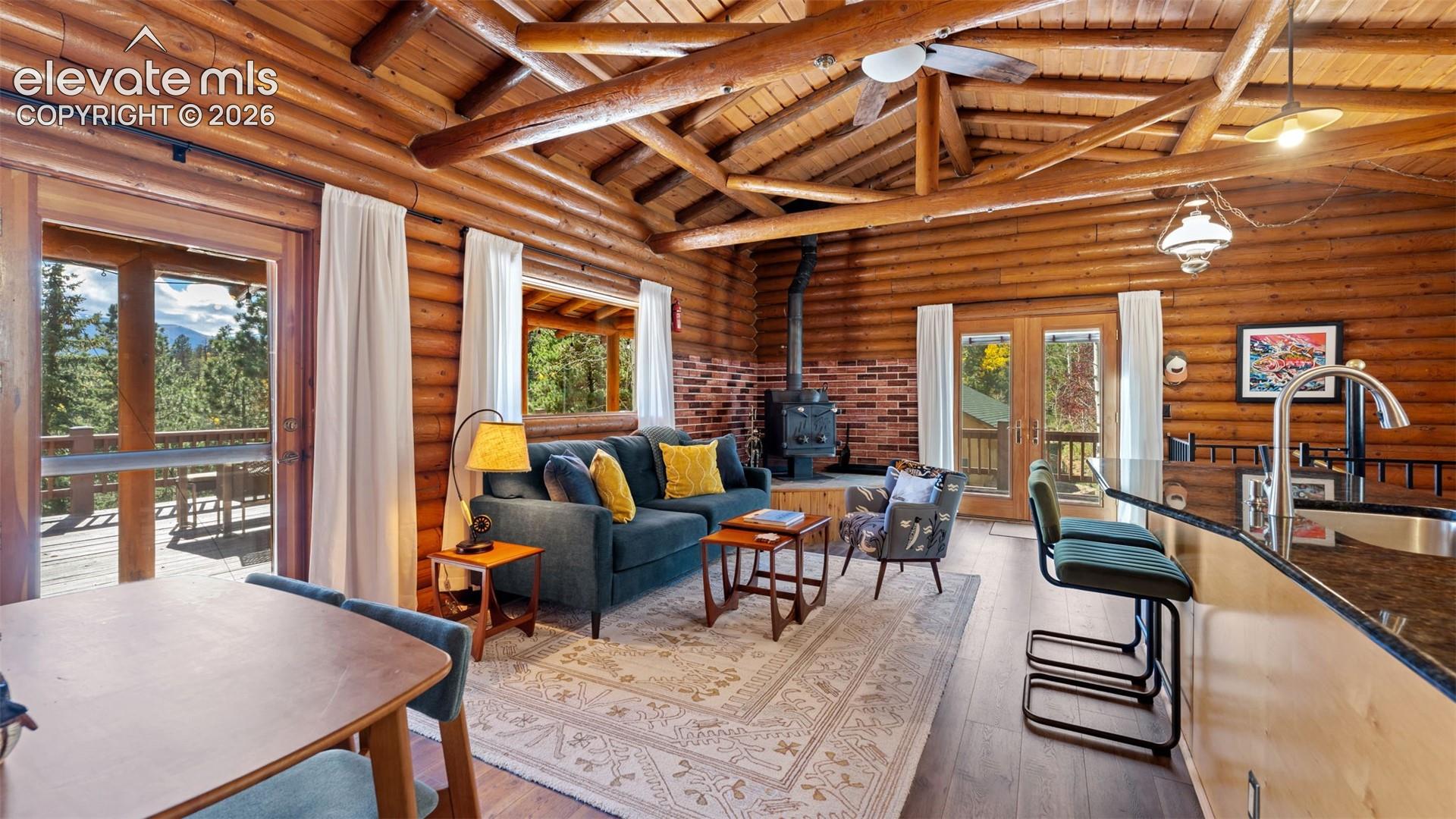 Log-walled interior featuring an exposed beam cathedral ceiling, brick hearth with a wood-burning stove, solid-surface breakfast bar, and dual glass-paneled doors