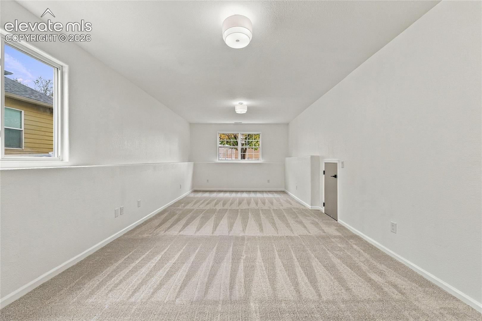 Neutral-toned carpeting, two dual-aspect windows, flush-mount ceiling lighting, and a dedicated storage access door