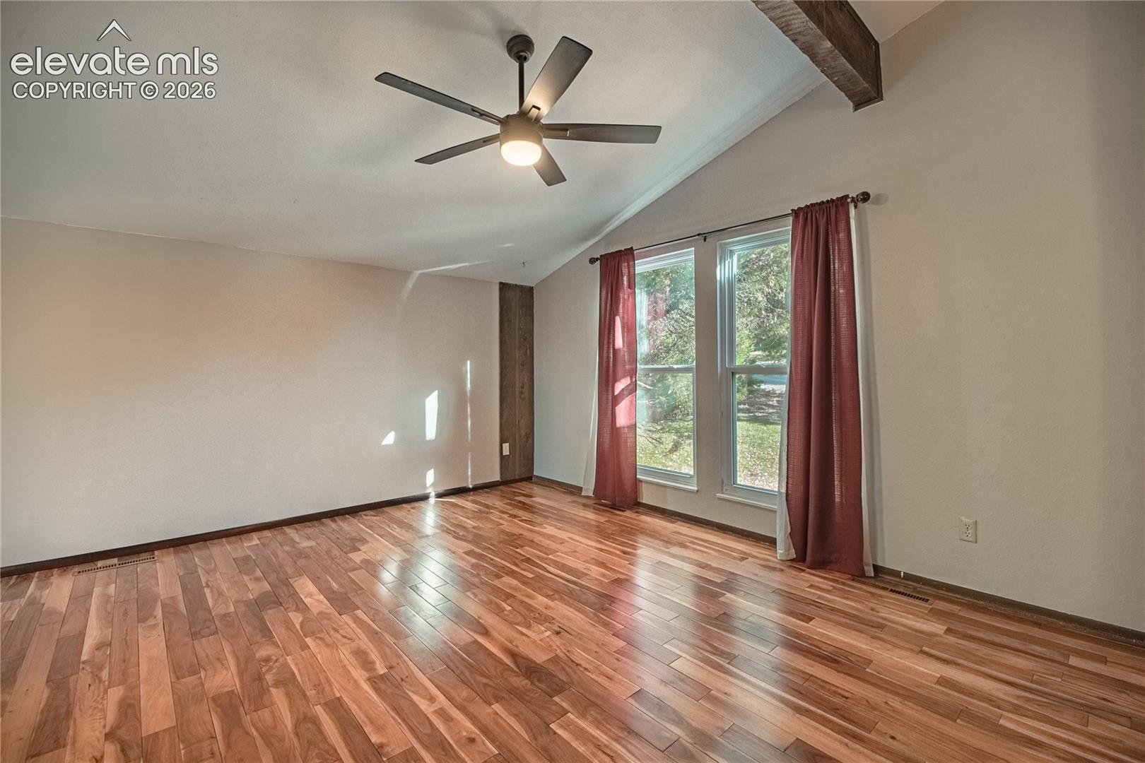 Vaulted ceiling with exposed wood-finish beam, wood-finish flooring, and ceiling fan with integrated lighting