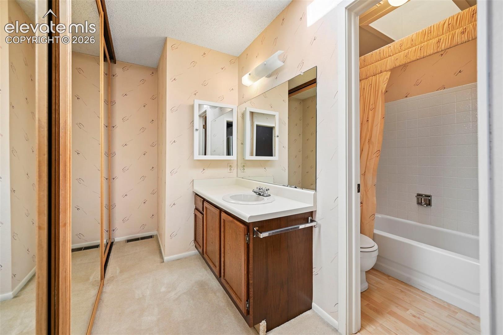 Bathroom featuring a wood-finish vanity with countertop, wall-mounted mirror, and mirrored sliding closet doors