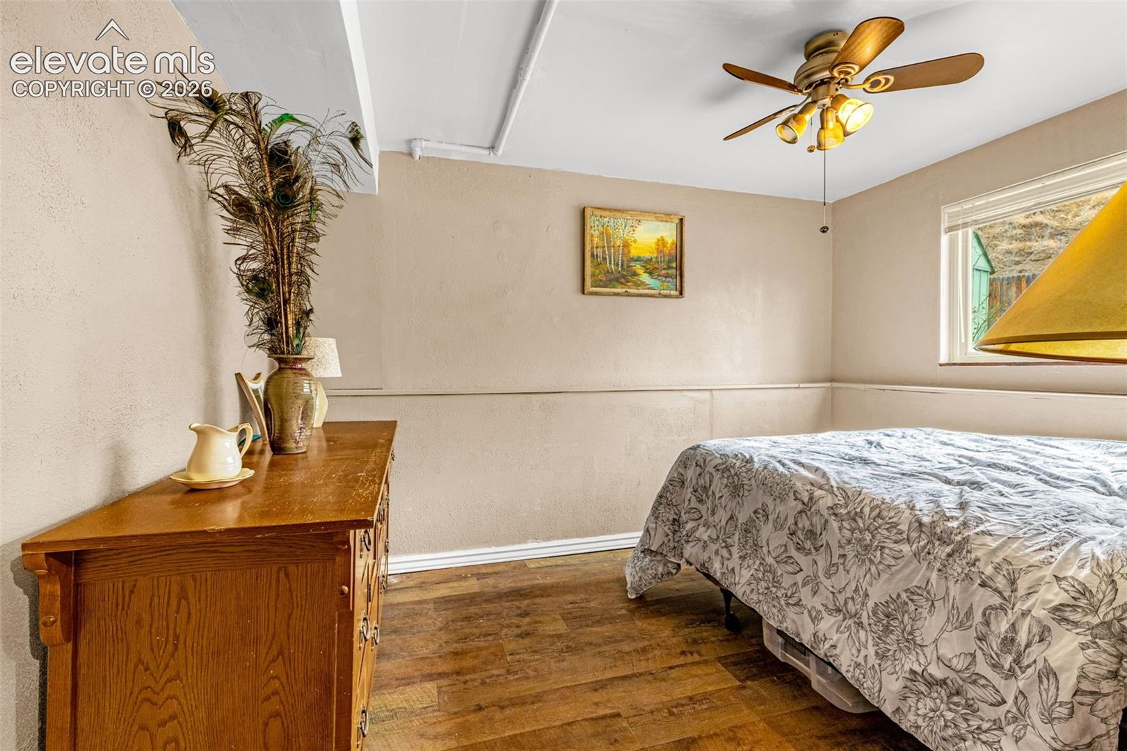 Wood-finish flooring, ceiling fan with integrated light fixture, horizontal window, and neutral wall tones with mid-wall trim detailing