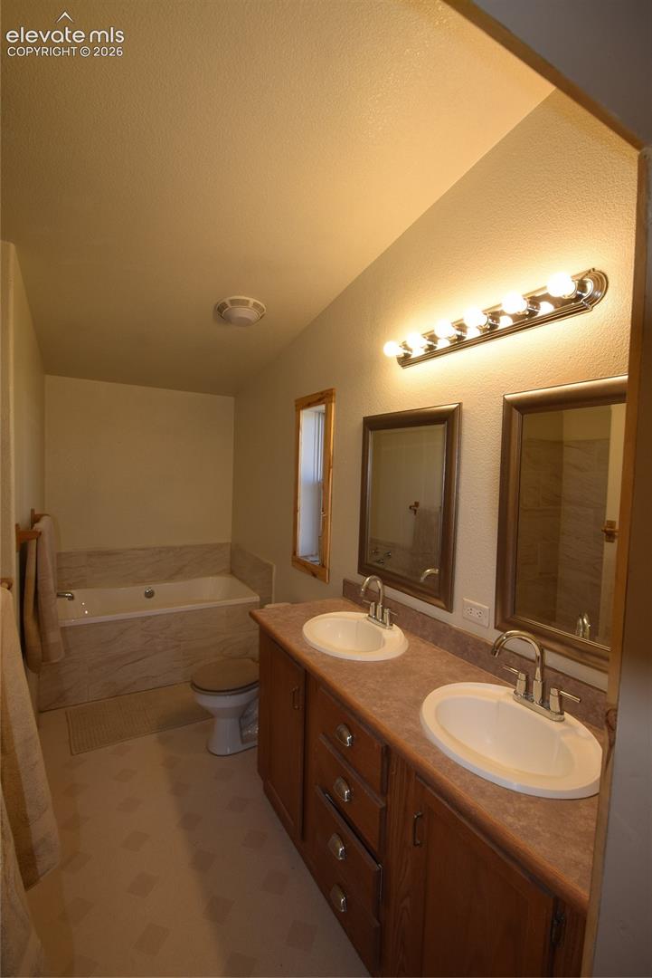 Double vanity with integrated sinks, wood-finish cabinetry, countertop, and a built-in bathtub with a tile surround