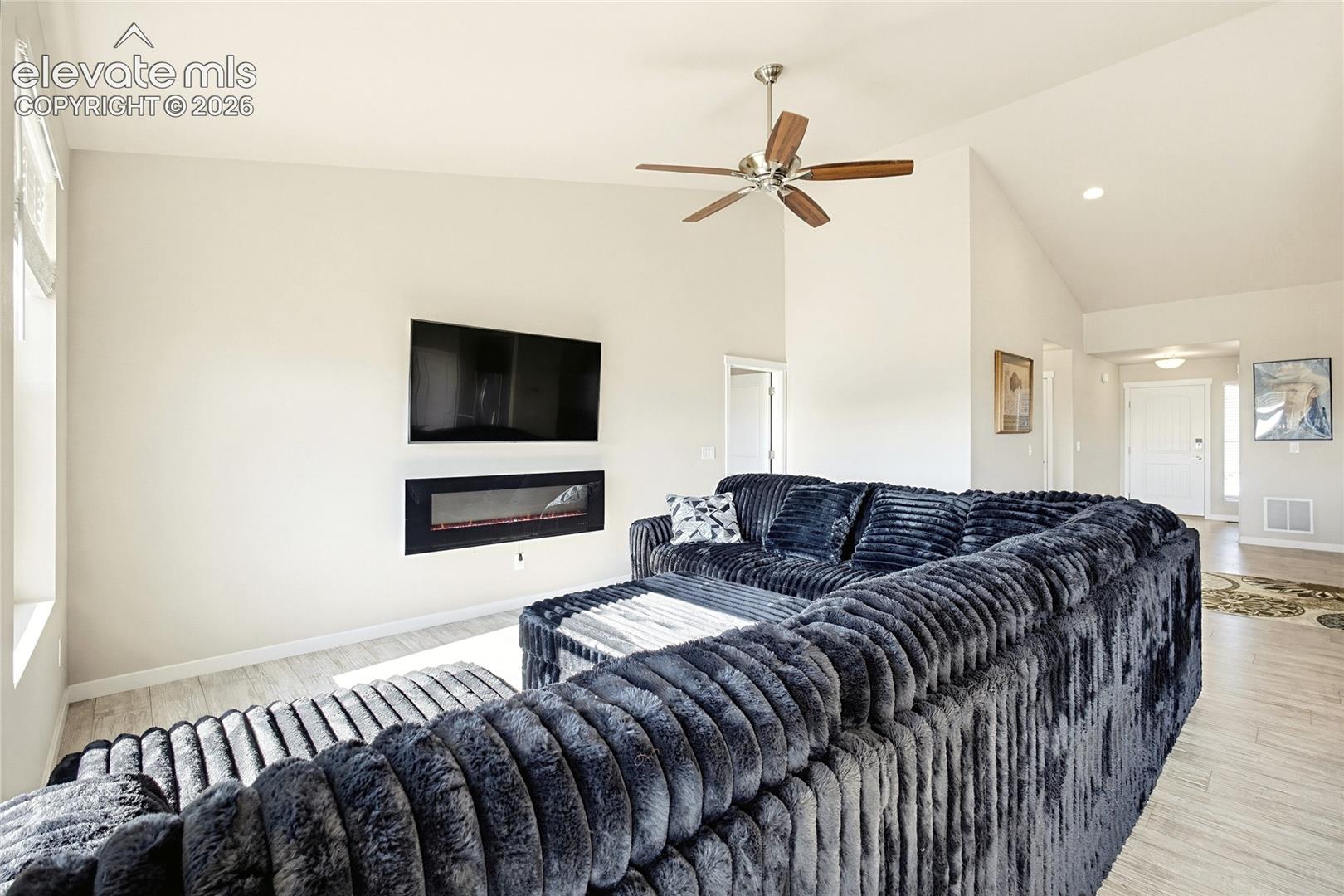 Vaulted ceiling featuring a ceiling fan, recessed lighting, wood-finish flooring, and a wall-mounted electric fireplace