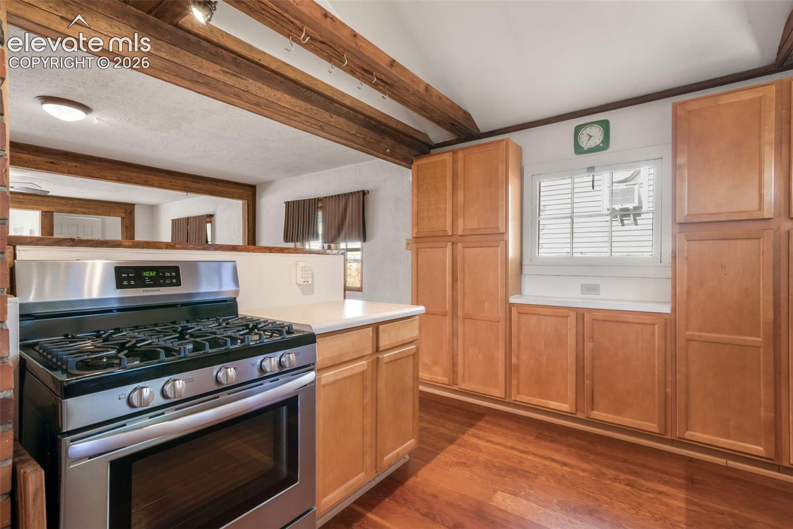 Stainless steel range with a gas cooktop, light wood cabinetry, white countertops, exposed wood beams, and wood-finish flooring