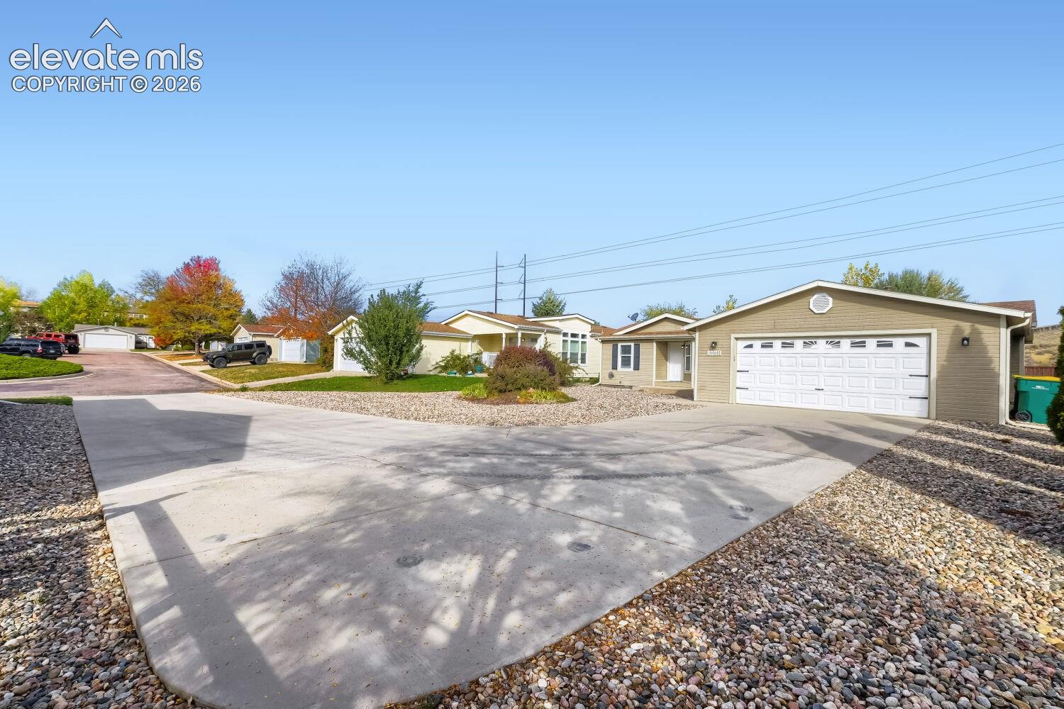 Exterior of a single-story residence featuring light-toned siding, an attached two-car garage with a sectional door, and an expansive concrete driveway with low-maintenance rock landscaping
