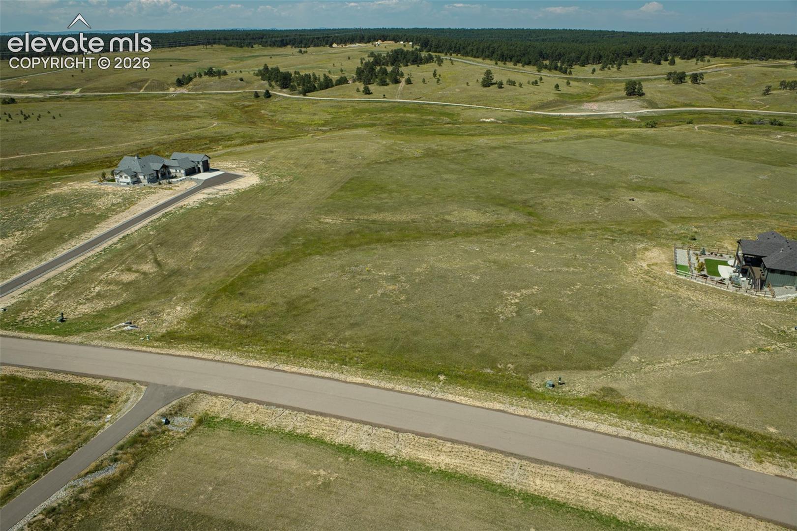 Expansive undeveloped acreage featuring paved road access and rolling topography, bordered by dense woodlands