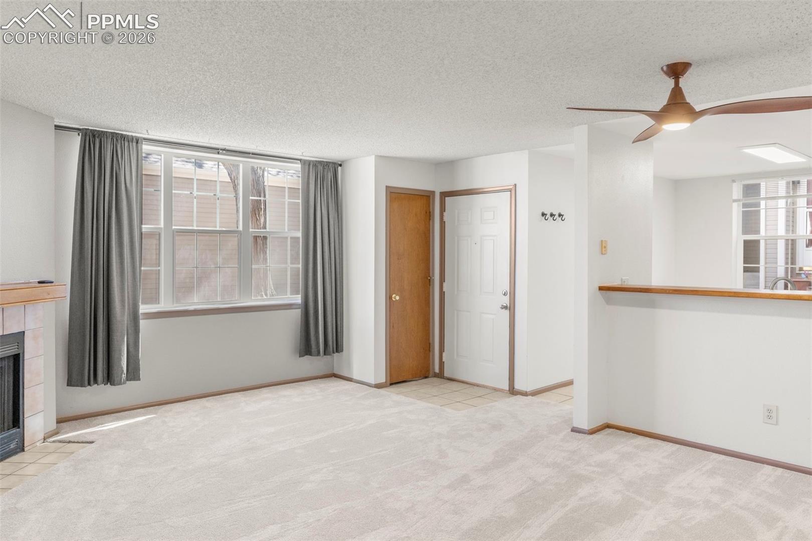 Unfurnished living room with a tile fireplace, light colored carpet, a textured ceiling, ceiling fan, and healthy amount of natural light