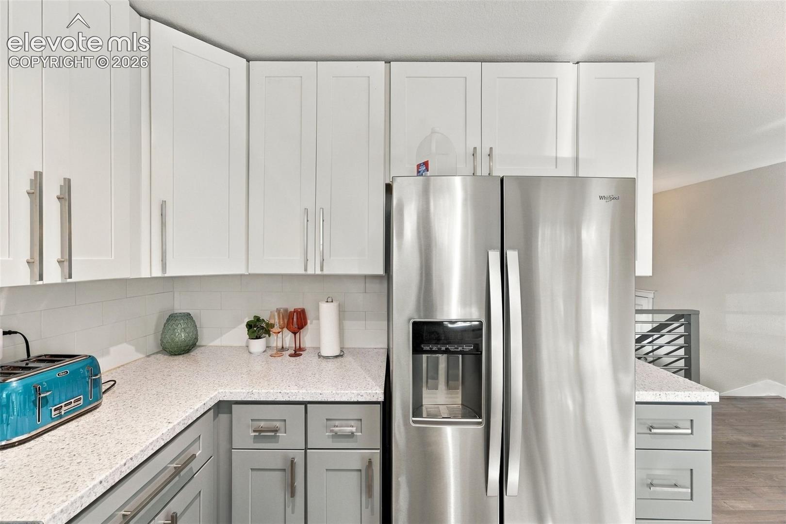 Stainless steel side-by-side refrigerator, white upper cabinetry, grey lower cabinetry, light speckled countertops, and a white subway tile backsplash