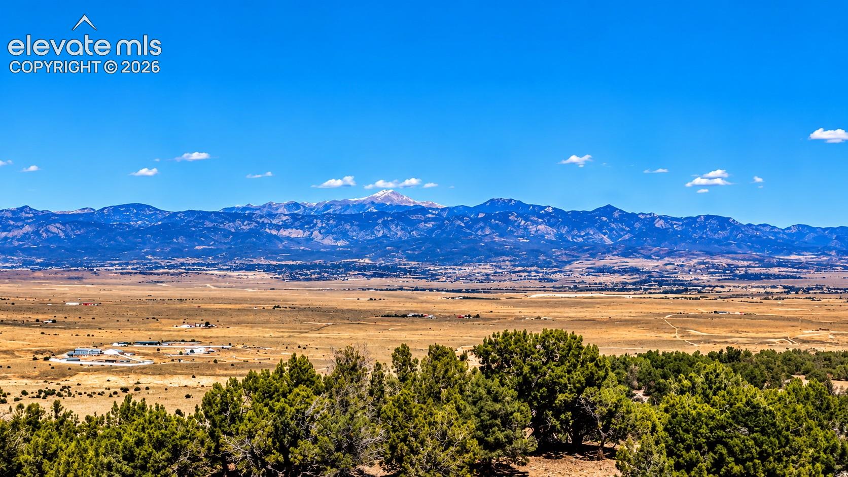 Stunning mountain views rise above a landscape of mature juniper trees, rolling hills, and natural Colorado vegetation.

