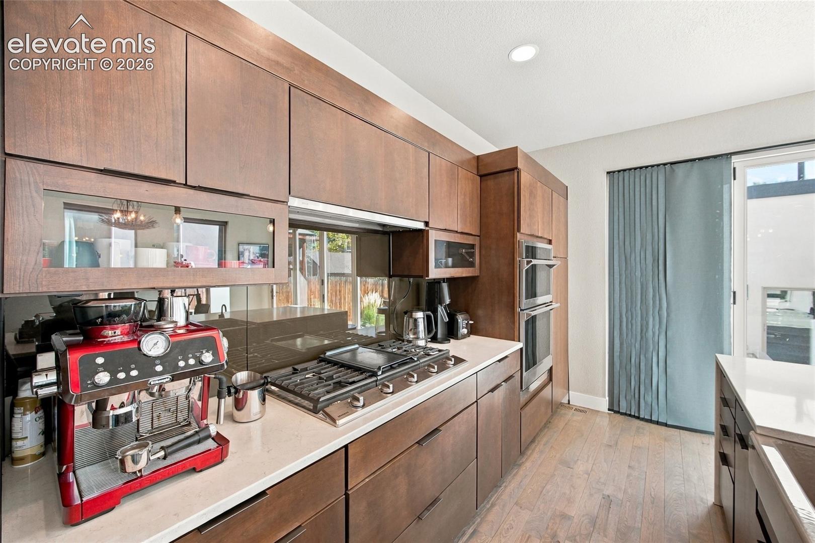 Custom flat-panel cabinetry, quartz countertops, integrated gas cooktop, and built-in ovens