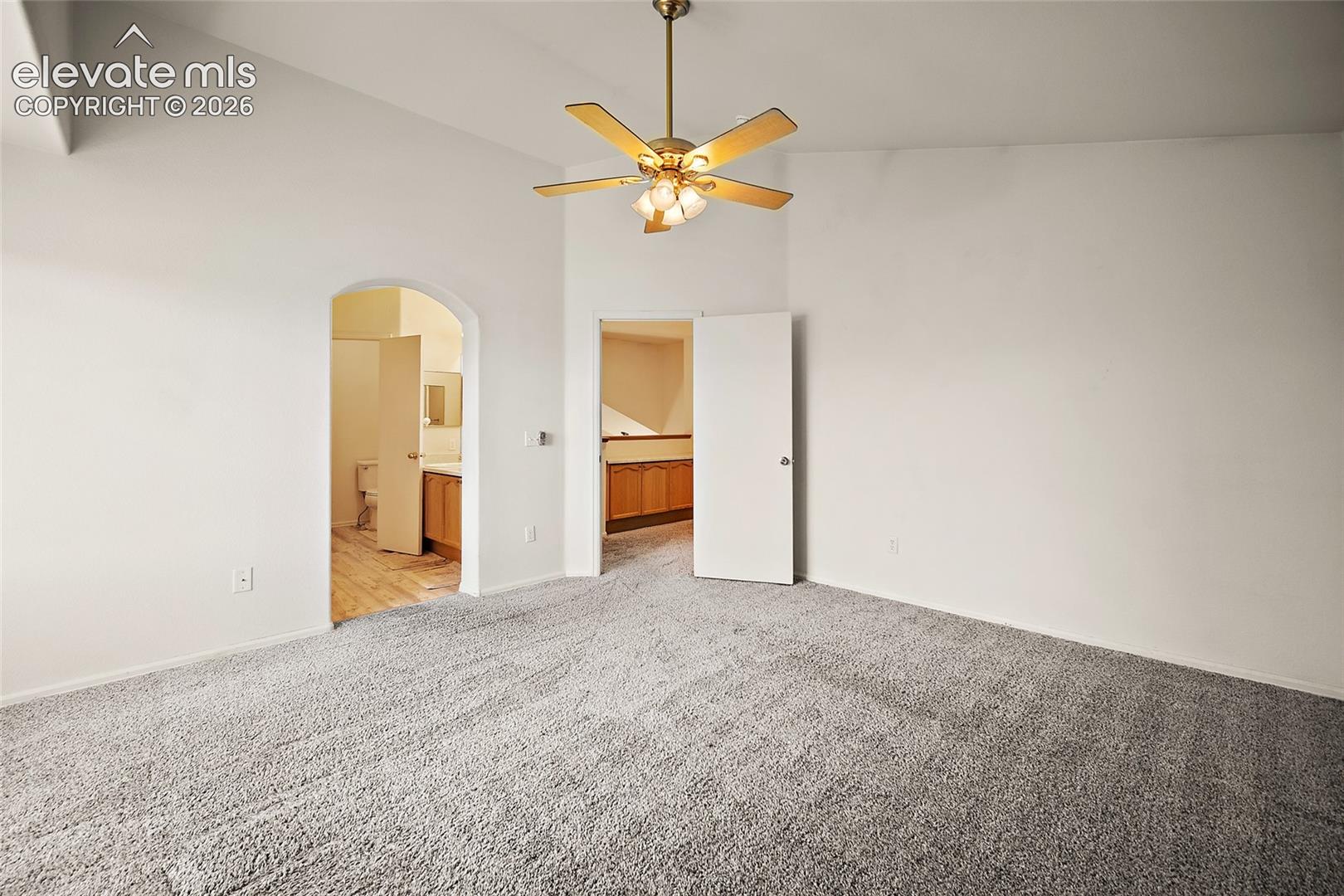 Spacious room featuring vaulted ceilings, a brass-finish ceiling fan with integrated lighting, and plush grey carpet flooring