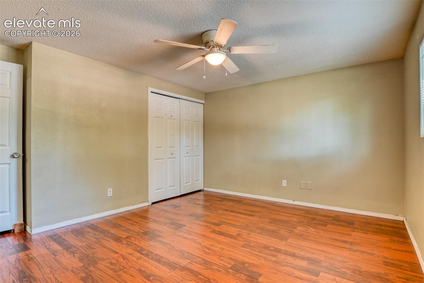 Spacious room featuring wood-finish flooring, a ceiling fan with integrated lighting, and a closet with bifold doors