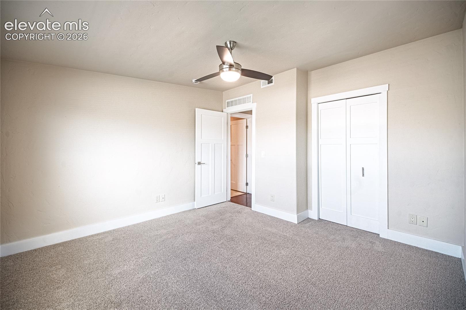 Spacious room with neutral-toned walls, plush carpet flooring, a modern ceiling fan with integrated lighting, a white paneled door, and a white bi-fold closet