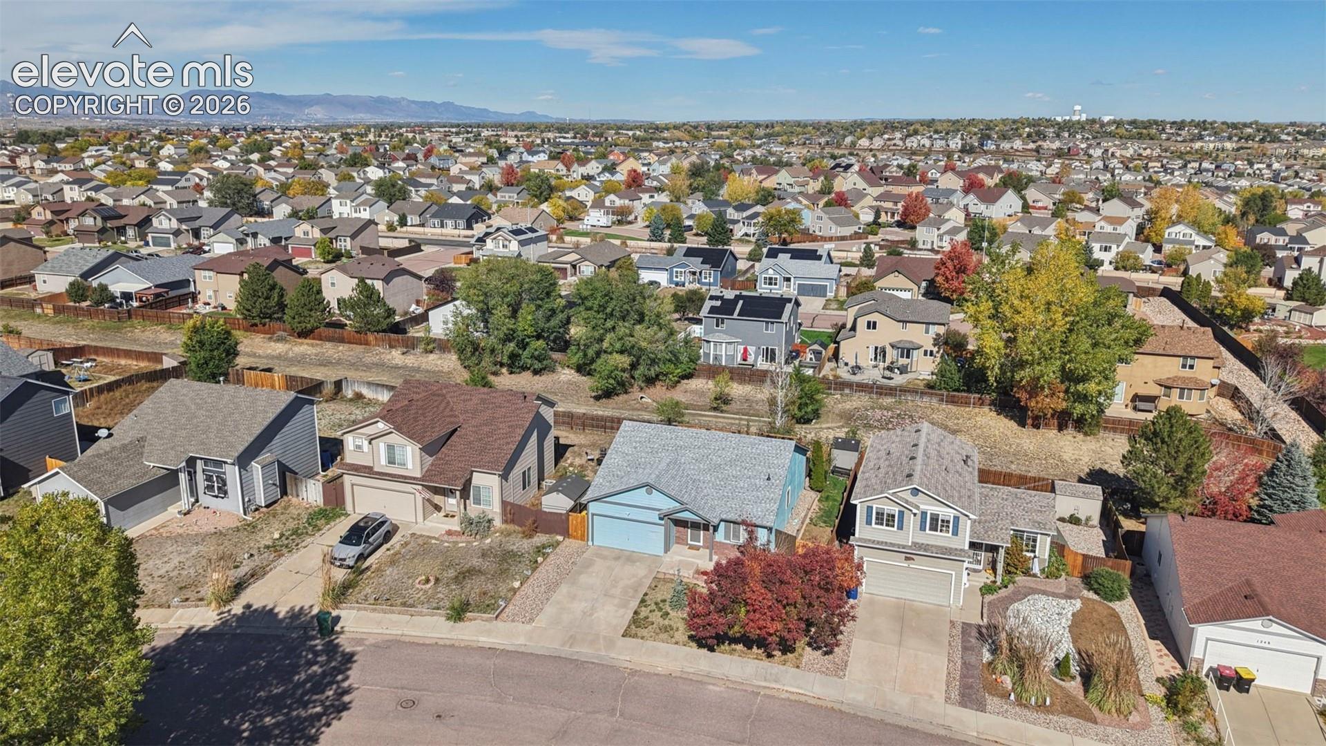 Aerial perspective of a suburban neighborhood featuring residential dwellings, established trees, and mountain silhouettes