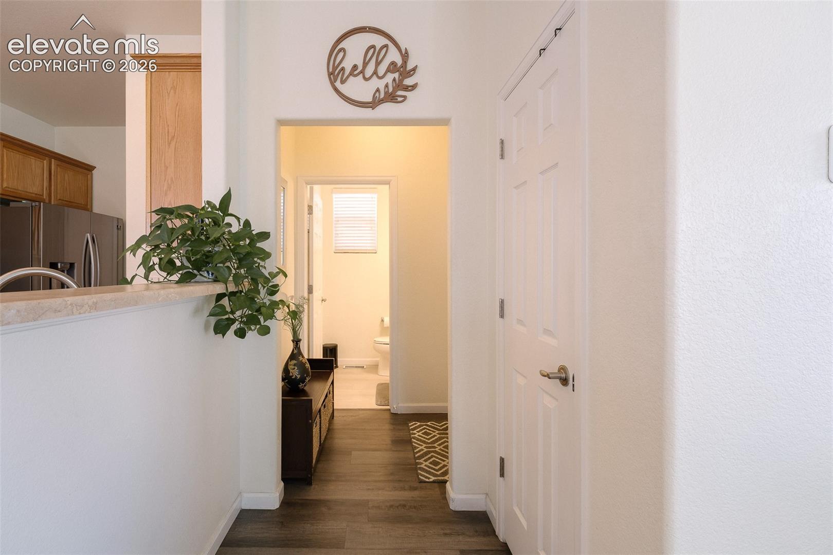 Hardwood-style flooring throughout, white interior walls, kitchen with wood-finish cabinetry and stainless steel appliances, and a powder room with window blinds
