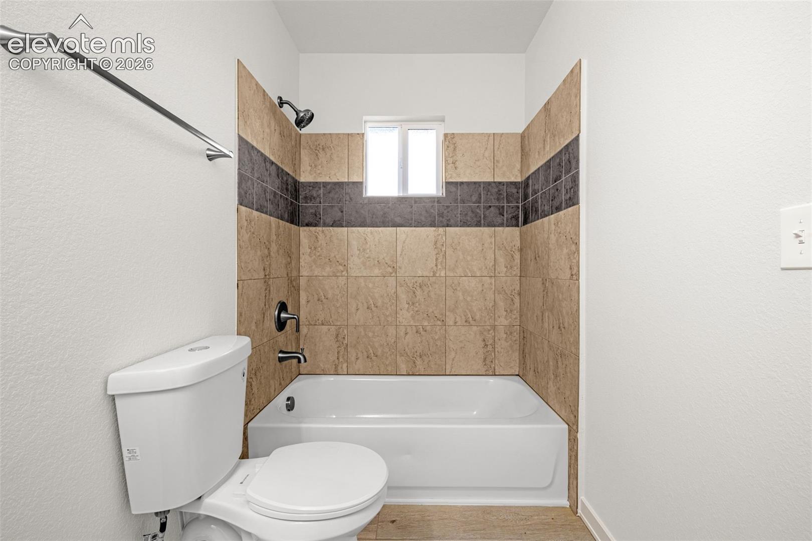Bathroom featuring a white tub, shower with dark bronze fixtures, and a tiled surround with a horizontal accent band
