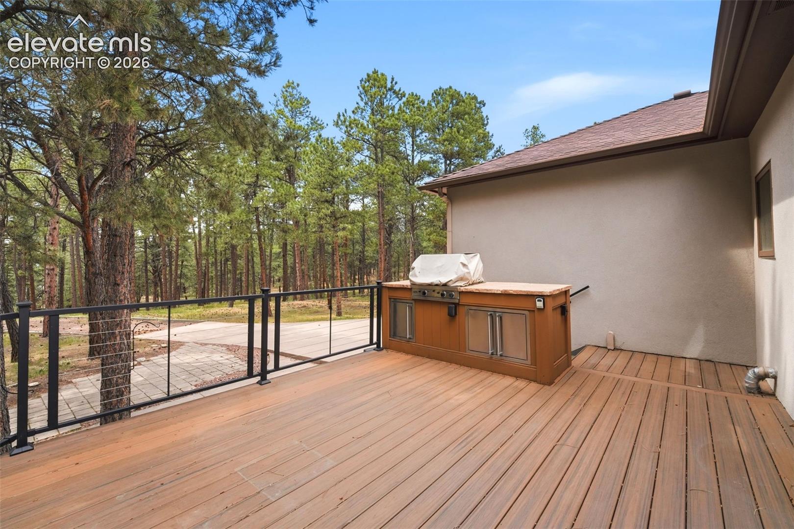 Expansive outdoor deck featuring wood-finish flooring, a contemporary black metal railing, and a built-in outdoor kitchen with a grill