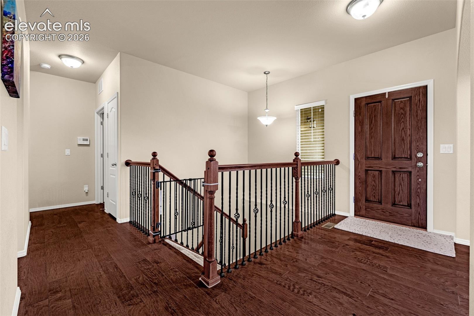 Entryway featuring wood-finish flooring, a solid wood six-panel front door, and a staircase with stained wood newel posts and ornamental metal balusters