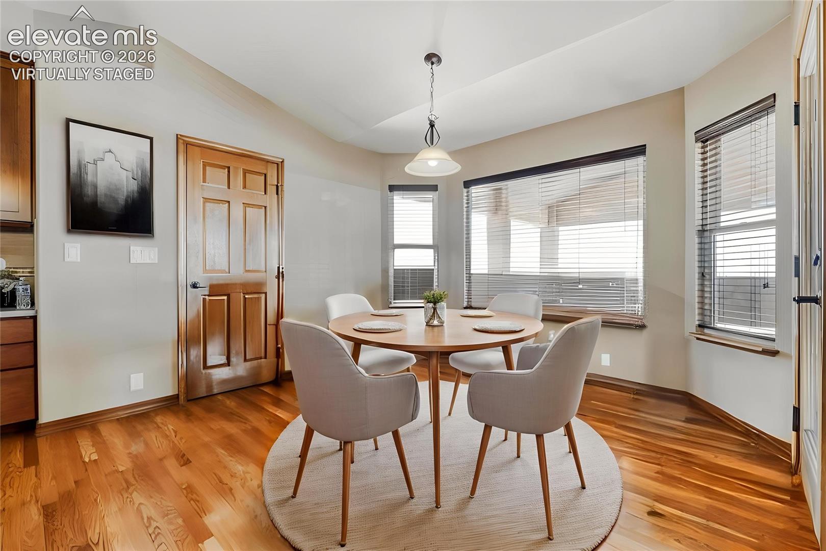 Virtually Staged - Dining area featuring wood-finish flooring, multiple windows with blinds, a prominent light fixture, and a paneled wood door