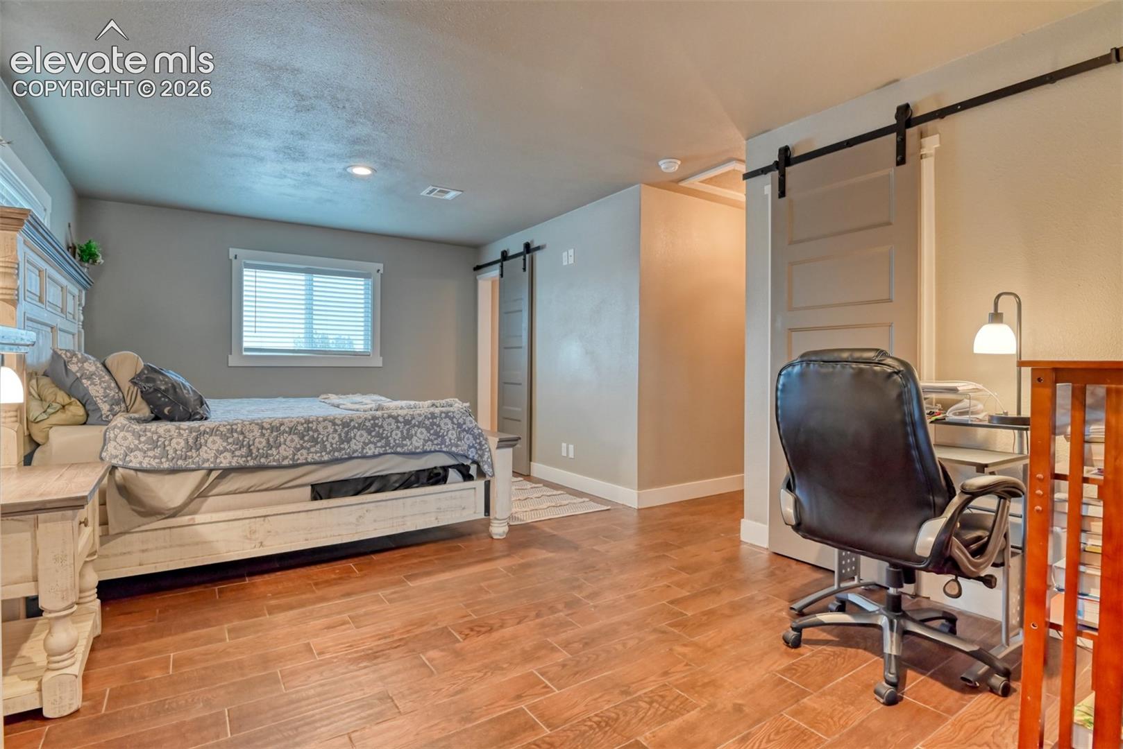 Bedroom with a barn door, light wood-style floors, and a textured ceiling