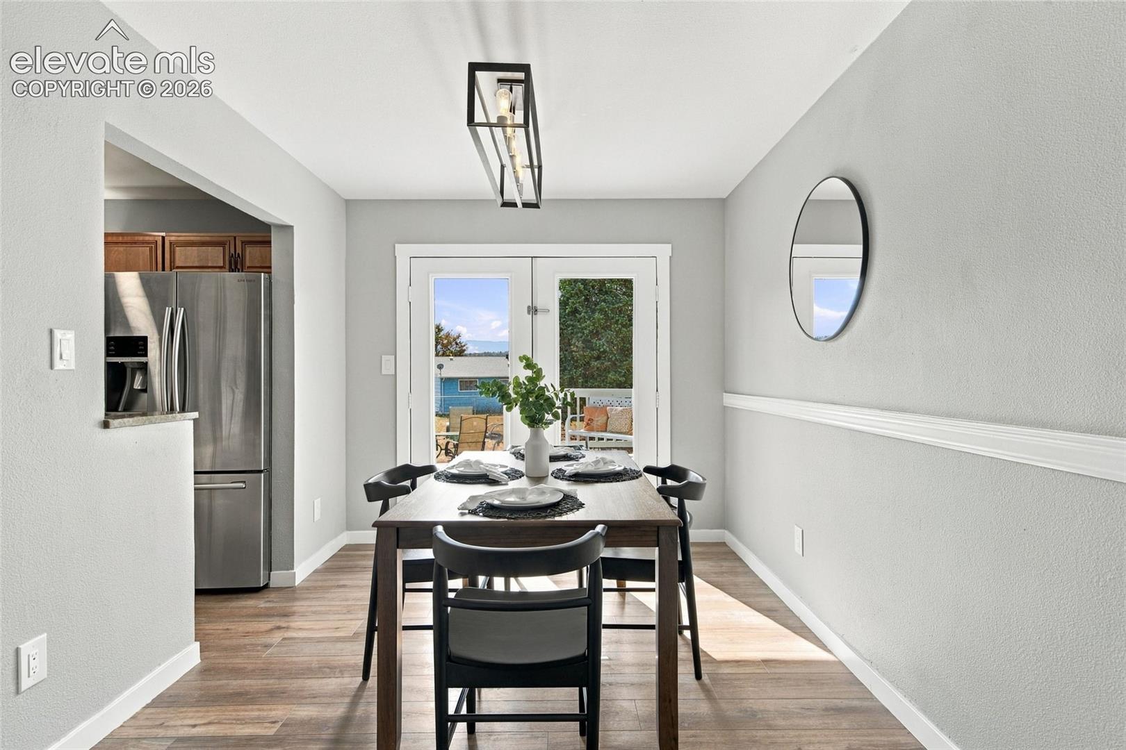 Dining area featuring wood-finish flooring, chair rail molding, a modern linear pendant light fixture, and double glass doors