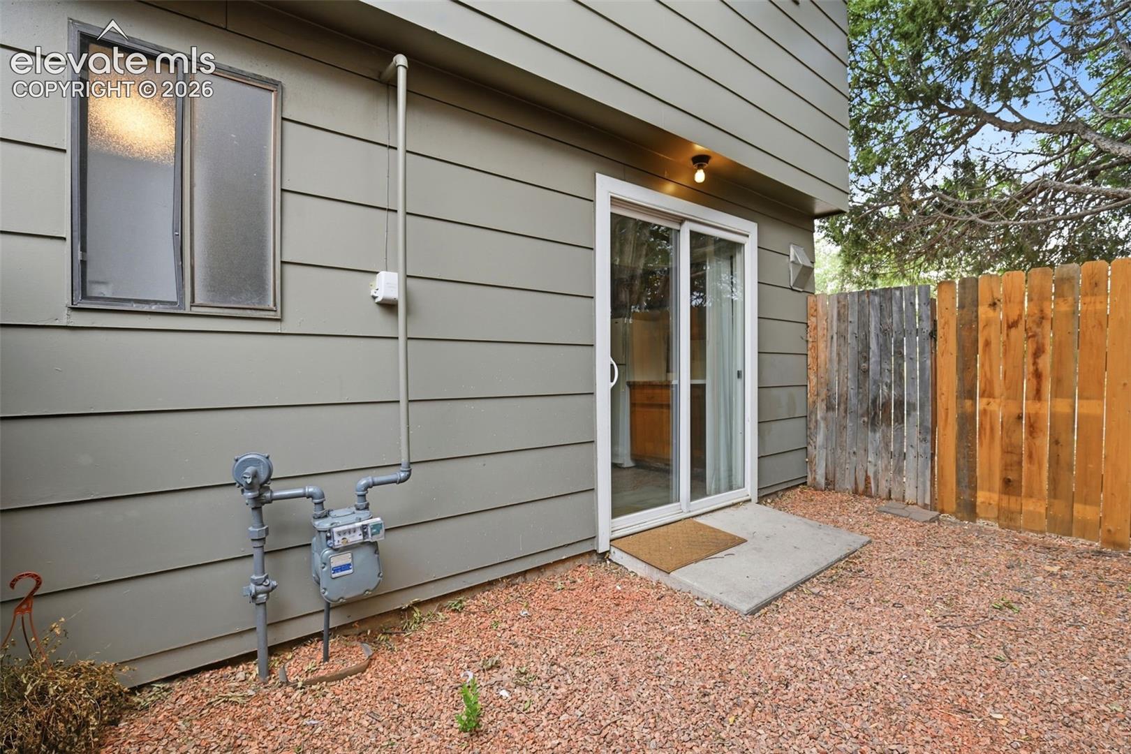 Sliding glass door entry, concrete landing, horizontal siding, gravel ground cover, and wood privacy fence