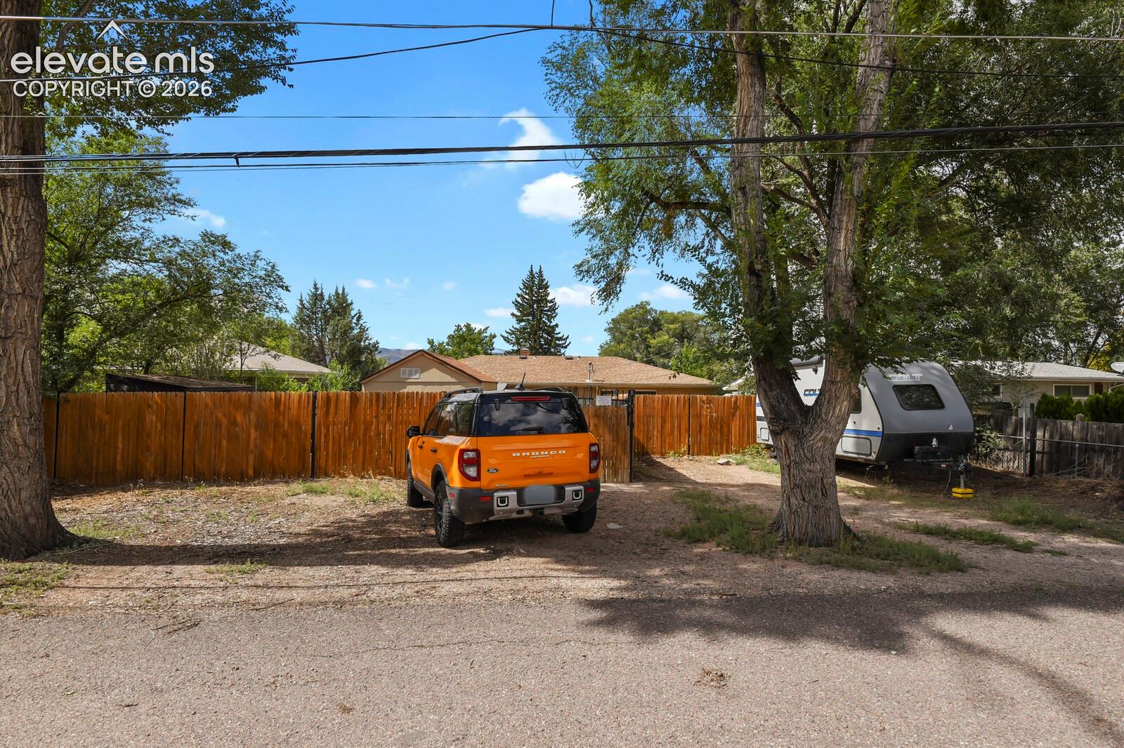 Gravel driveway with mature trees and wood fence