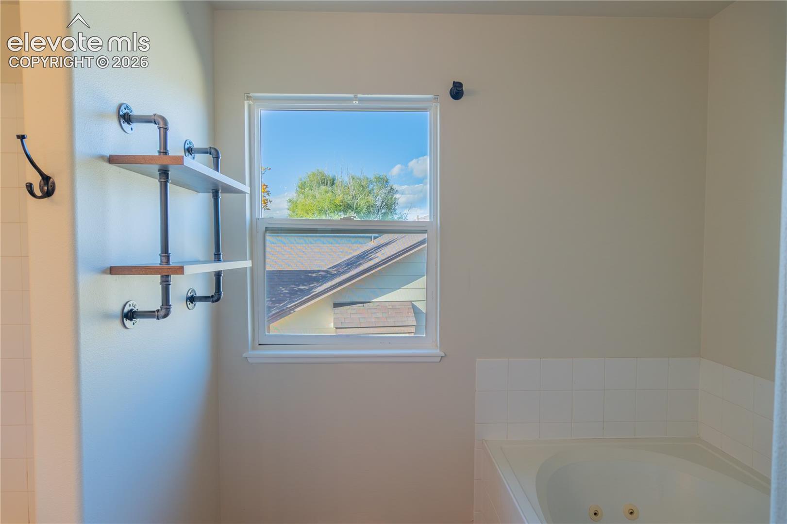 Relax in the jetted soaking tub, surrounded by tile and natural light from the nearby window.