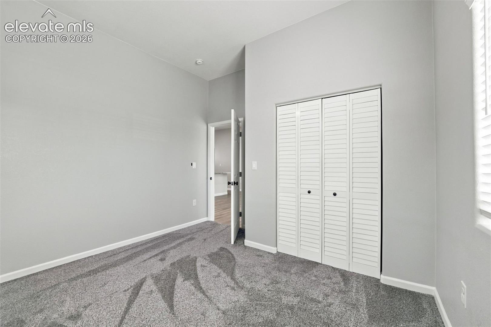 Gray carpeted flooring, light gray wall paint, white louvered bifold closet doors, white baseboards, and a recessed ceiling light