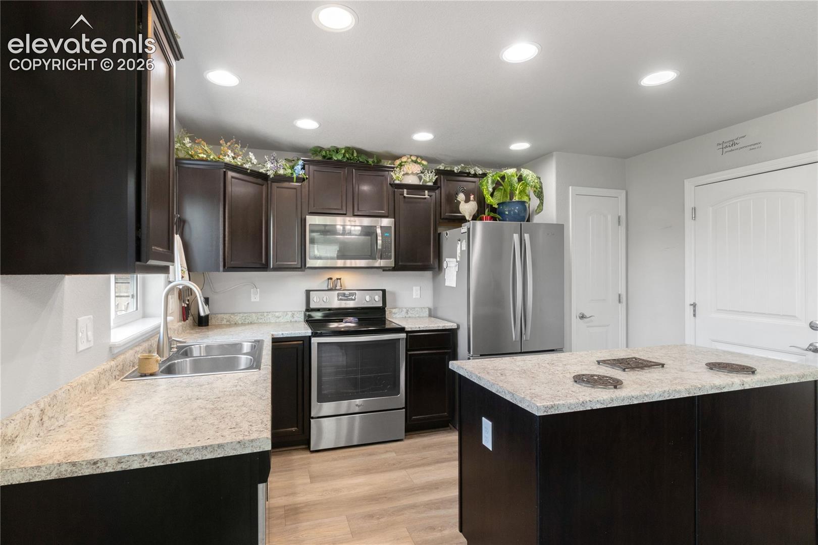 Dark wood-finish cabinetry with stainless steel appliances, light-toned countertops, and wood-finish flooring
