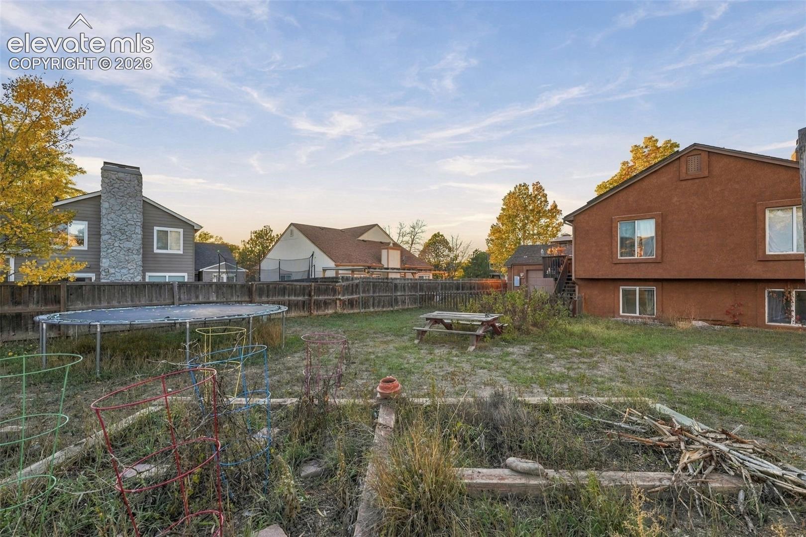 Spacious backyard featuring a perimeter wood fence, raised garden beds, and mature trees